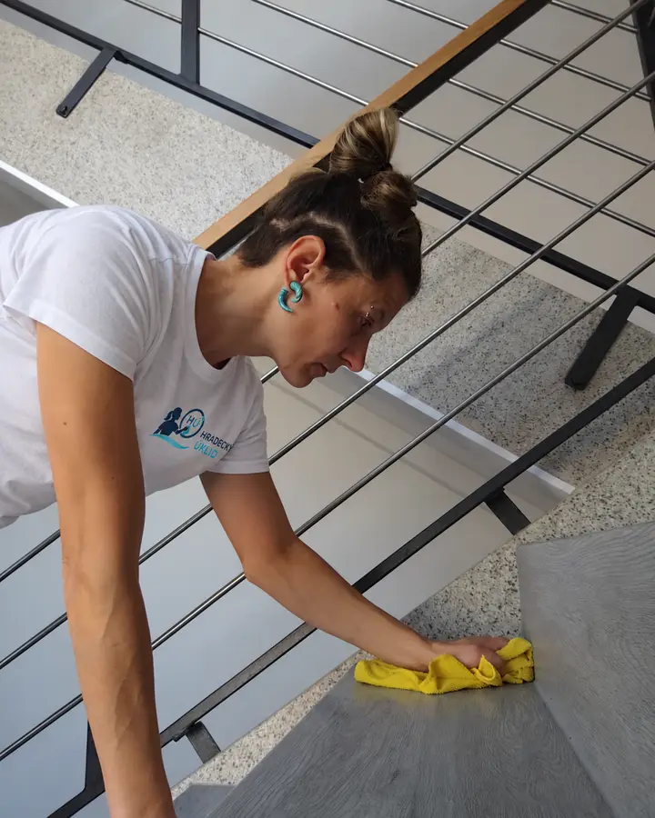 Marie Coufalová utírá prach ze schodů a zábradlí